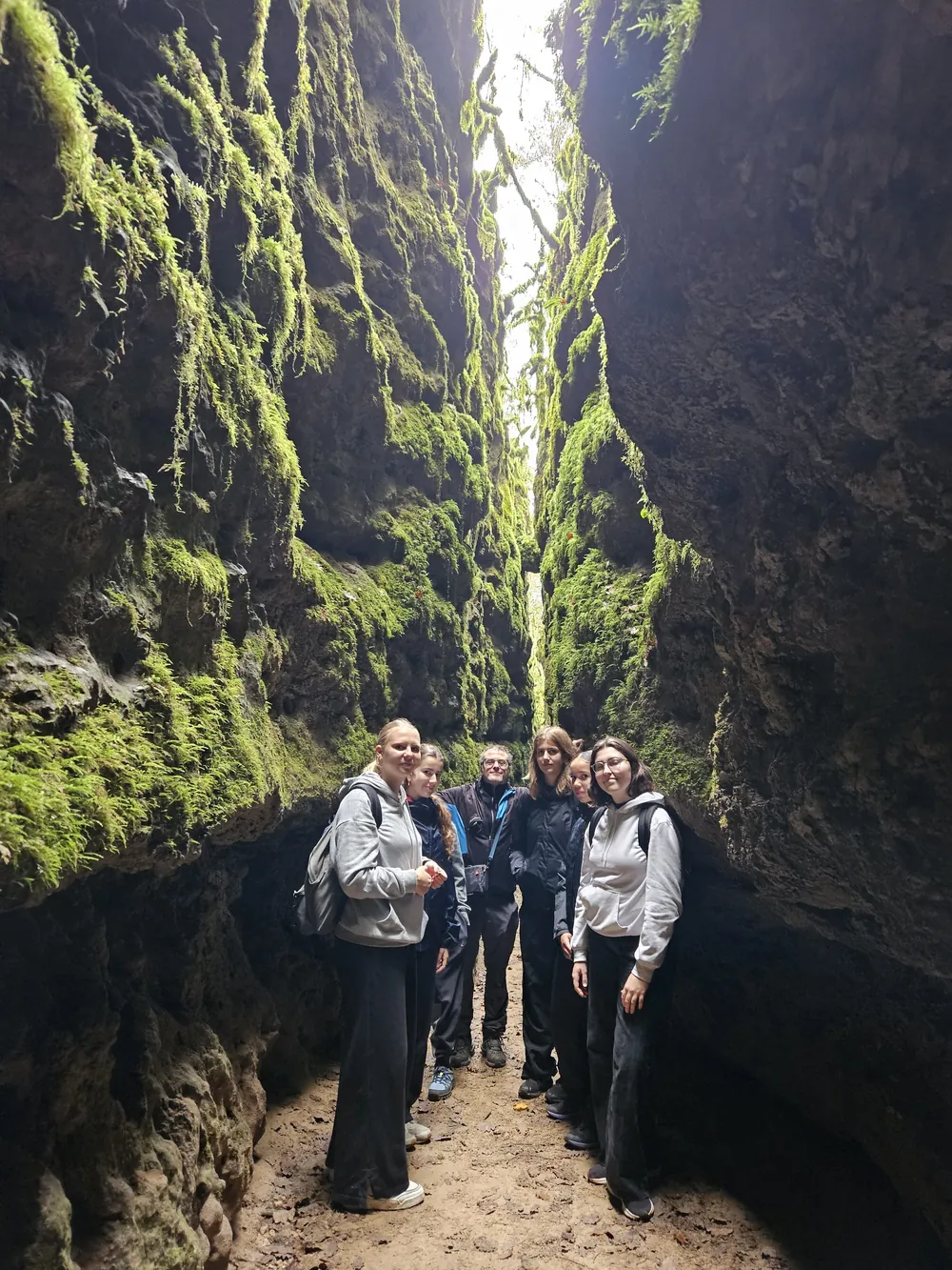 Randonneurs dans un passage étroit aux parois de pierre couvertes de mousse