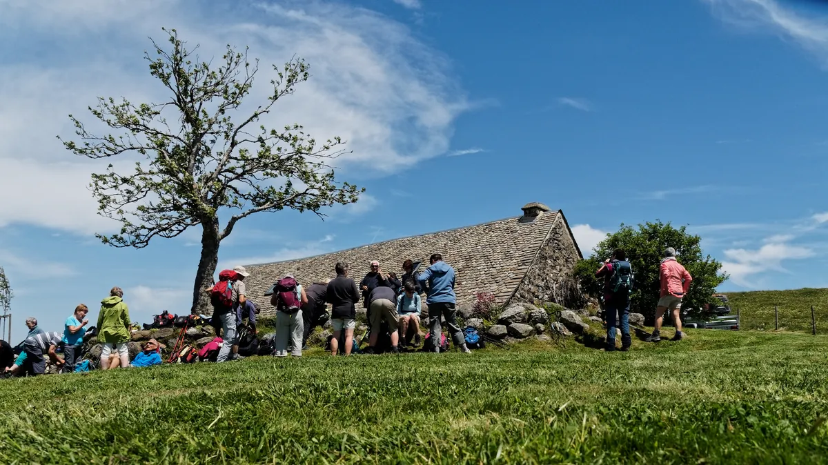 Groupe de randonneurs sur le causse, au pied d'une bergerie en pierre